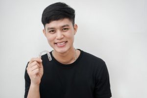 young man smiling holding invisalign tray